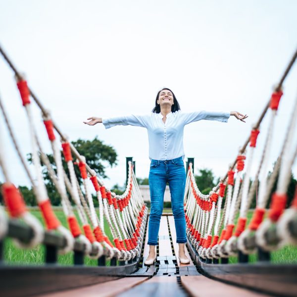A happy woman on a wooden bridge in a green meadow on a sunny day. Happy, health, travel, lifestyle concept