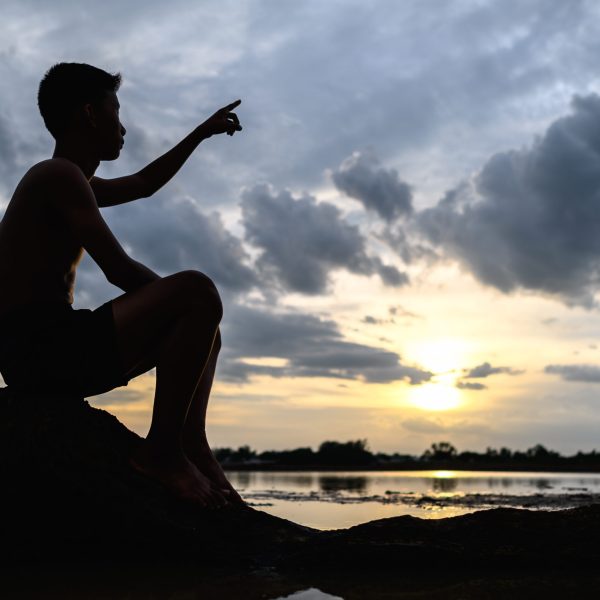The man was sitting on the base of the tree, placing his hands pointing forward during the sunset.