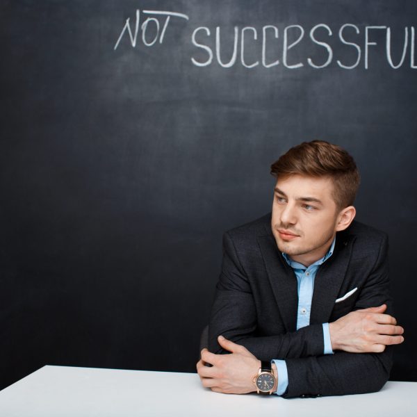Picture of a  suited, sad man over black board with a text successful. Looking left.
