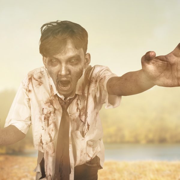 Scary zombie with blood and wound on his body walking on the field