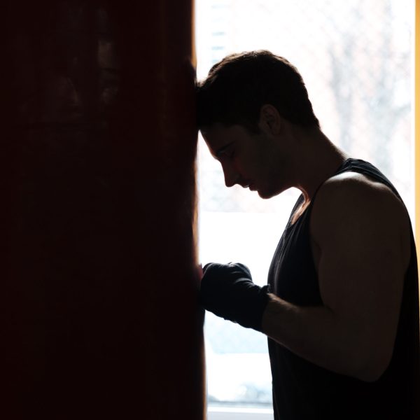 Tired sportsman boxer leaning on red punchbag while training